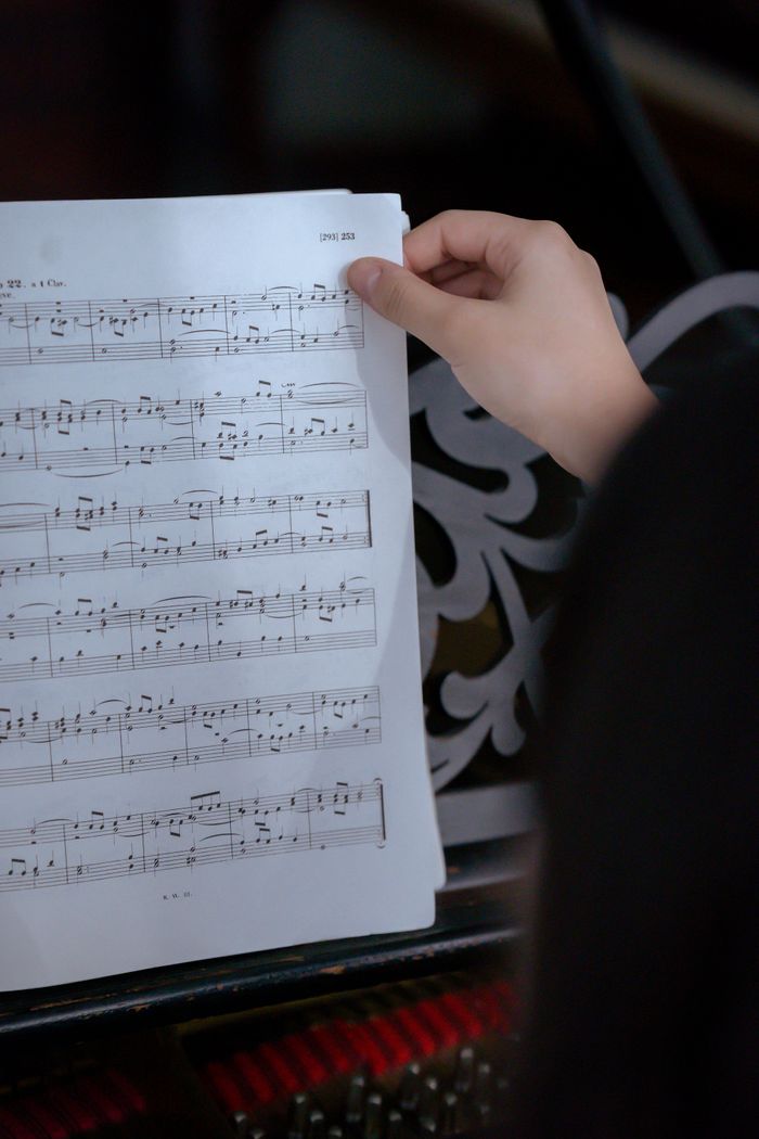 services-03 Crop unrecognizable female musician turning page of music book with notes near piano in light classroom